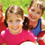 Three children smiling in a field.